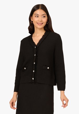 Cardigan noir texturé avec un col en V, des bords effilochés et une fermeture à boutons sur le devant. Dispose de deux poches avant avec des accents de boutons en argent.