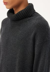 Dunkelgrauer Rollkragenpullover aus weicher Wolle, mit einem gerippten Kragen und einem leicht lockeren Schnitt, der eine glatte, strukturierte Oberfläche aufweist.