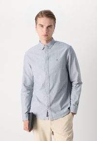 Φωτεινό μπλε πουκάμισο με κουμπιά, φτιαγμένο από μαλακό ύφασμα, που έχει ένα μικρό λογότυπο στη θήκ�η του στήθους, με μακριά μανίκια και κλασικό γιακά.