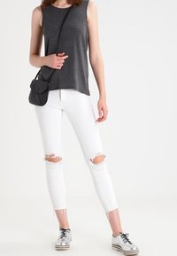 Grå ärmlös topp, vita rivna skinny jeans och silverfärgade snörskor. Liten svart crossbody-väska. Enkel, avslappnad outfit.