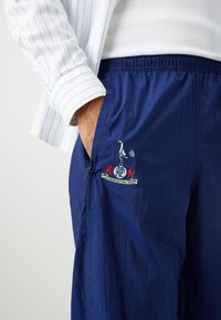 Marineblaue, leichte Shorts mit elastischem Bund und Seitentaschen, versehen mit einem gestickten Logo mit einem Vogel und roten Akzenten.
