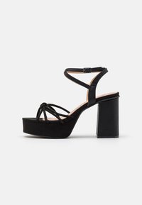 Sandali platform neri con tacco chunky. Presentano un design a strap incrociati e un accento annodato sulla punta. Realizzati in materiale scamosciato.
