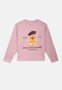 T-shirt de manga longa rosa com um gráfico de um urso de pelúcia a usar uma boina, com texto que inclui "Não te preocupes, sê urso" e "EST. 1986."