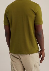 Olivgrön kortärmad t-shirt, texturerad tyg, rundad halsringning, sidofickor, matchad med beiga cargobyxor, visad bakifrån.