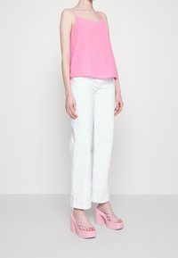 Pink silk tank top with thin straps, paired with white wide-leg trousers and chunky pink heeled sandals featuring a woven design.