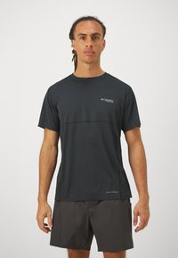 Camiseta atlética negra de manga corta con cuello redondo, fabricada en un material ligero, con diseño texturizado y logo en el pecho. Combinada con pantalones cortos oscuros.