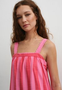 Robe sans manches rayée rose avec des bretelles texturées et festonnées. Présente une coupe décontractée avec un tissu doux et fluide ainsi qu'un corsage froncé.