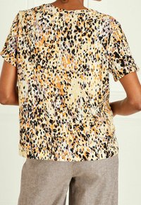 Korte mouw top in lichtgewicht stof met een geel, oranje, paarse en zwarte dierenprint, met een ronde halslijn en subtiele textuur.