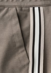 Beige stof met een diagonale zakopening en een verticaal gestreepte rand in beige, wit en zwart langs de rand.
