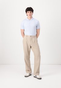 Light blue short-sleeve polo shirt, beige tailored pants, and black-and-white sneakers, standing on a plain background.