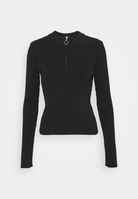 Pull-over noir à manches longues en maille côtelée avec un col montant et une fermeture éclair courte à l'avant dotée d'une tirette en métal ronde.
