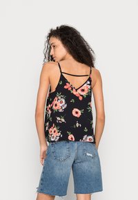 Top de algodão preto com flores, com alças finas, apresentando flores rosas e brancas. Usado com calções de ganga azuis, exibindo um estilo casual e folgado.