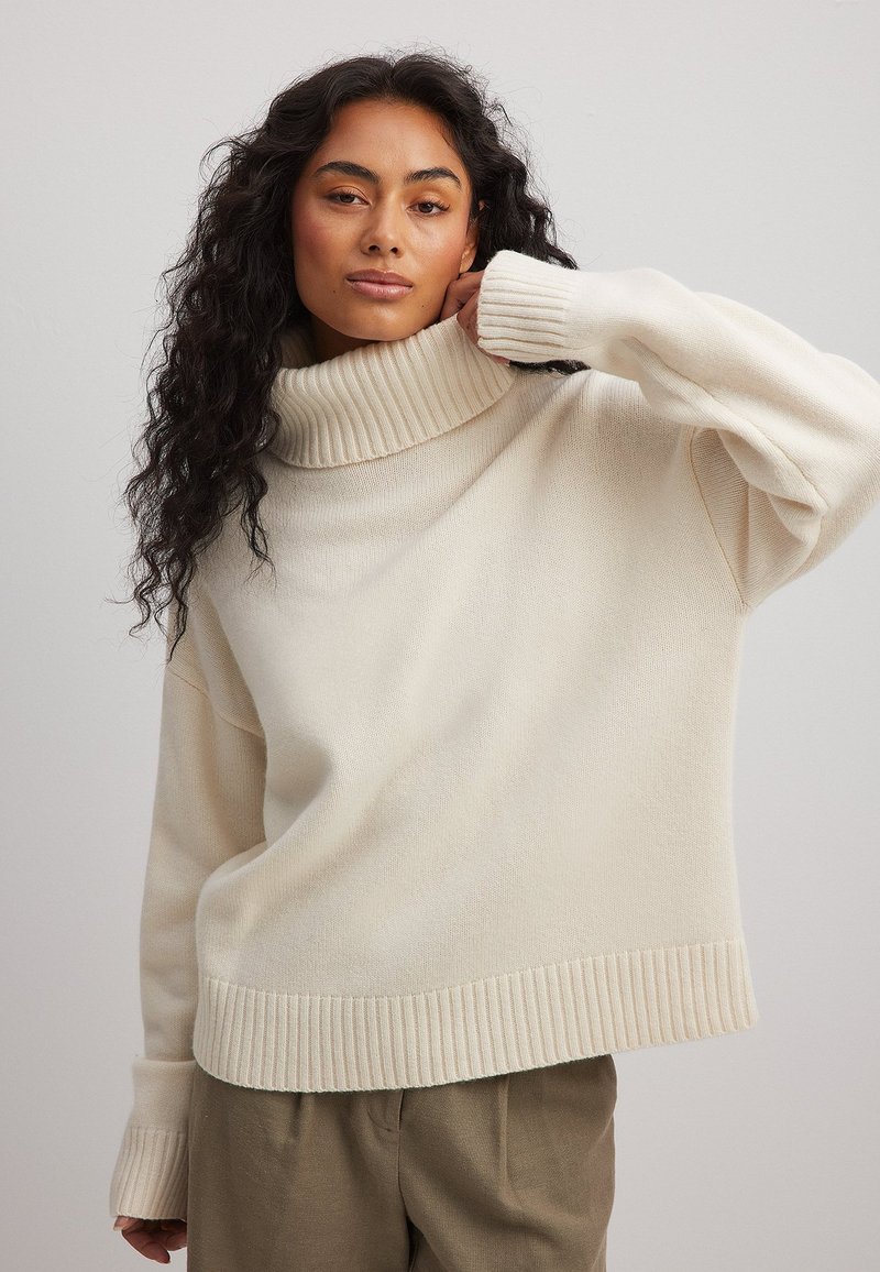 Kremkrāsas džemperis ar augstu ribotu apkakli, brīvu piegriezumu, nolaišanām pleciem un ribotām piedurknēm un apakšmalu. Mīksta, teksturēta auduma.