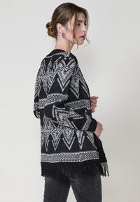 Cardigan a righe bianco e nero con disegni geometrici, dotato di frange all'orlo e maniche lunghe, realizzato in materiale a maglia testurizzato.