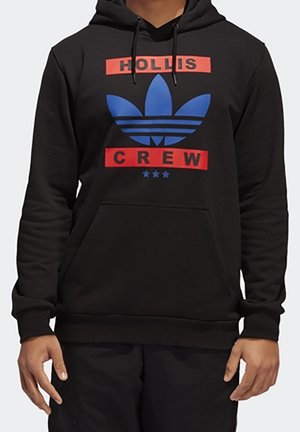 Czarna bluza z kapturem z niebieskim, stylizowanym logo liścia i czerwonym tekstem "HOLLIS CREW", noszona przez osobę stojącą z rozluźnionymi rękami.