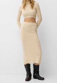 Béžový pletený crop top a midi sukně s ribovanými detaily, doplněné černými koženými vysokými botami s kovovými prvky.