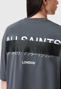 Šedé oversized tričko s bílým nápisem "ALLSAINTS", černým pruhem na zadní straně a textem v japonštině nad "LONDON" na spodní části.