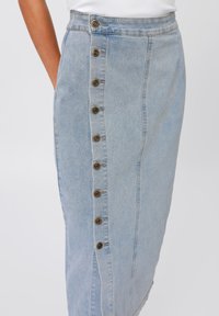 Lyseblå denimskjørt med rett silhuett, sideknapper og kontrasterende hvit søm. Har lommer for funksjonalitet.