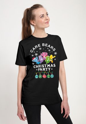 Sort t-shirt med farverigt Care Bears design, der har teksten "Christmas Party Cheer" og ornamentgrafik, vist på en model.