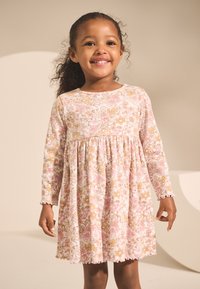 Klänning med långa ärmar i ljusrosa med ett blommönster i gult och rosa. Har en rynkad midja och vågformade ärmslut.