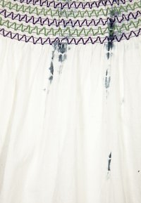 Bíl dresses s nařasenou texturou, se barevným vyšíváním v zelené a fialové barvě na linii krku. Obsahuje tmavé inkoustové skvrny.
