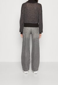 Maglione a maglia oversize nero e grigio a righe con collo alto; abbinato a jeans a gamba larga grigio chiaro, con leggeri dettagli di usura decorativa.