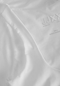 Fehér selyem anyag, lágy fényű, finom varrással és berakott márkanevével: "JJXX STUDIOS." Az "S" méret egyértelmű betűtípussal feltüntetve.