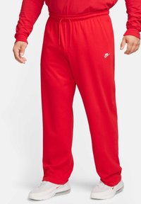 Piros Nike melegítőnadrág, elasztikus derékkal, állítható húzózsinórral és logóval díszítve. Az anyag puhanak tűnik, és lazán illeszkedik.