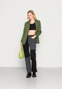 Blazer xadrez verde sobre um top cropped preto, combinado com calças cinza e pretas em bloco de cor. Inclui uma pequena carteira verde e botas pretas.