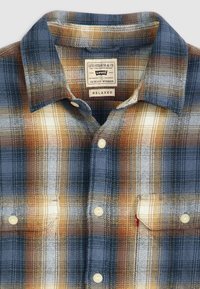 Camisa de cuadros para hombre en colores azul, marrón y crema. Fabricada en algodón con un corte relajado. Los detalles incluyen botones de perla y un bolsillo en el pecho.