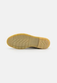 Suela de zapatilla de goma en beige con un patrón de tracción texturizado, que presenta el logo "bugatti" grabado en la entresuela y bordes suaves para un mejor agarre.