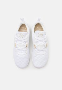 Pár bílých běžeckých tenisek Nike s pletenou texturou, béžovými stélkami označenými "Comfort Footbed" a bílými tkaničkami se zlatými očky.