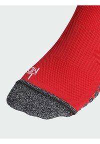 Κόκκινη κάλτσα με υφή στο σώμα και μαύρη patterned μύτη. Διαθέτει λείο δακτύλιο και λευκή λεπτομέρεια λογότυπου κοντά στον αστράγαλο.