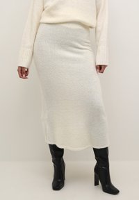 Strikket sæt bestående af sweater og nederdel i off-white, med en blød tekstur og ribbede ærmekanter, parret med sorte højhælede støvler.