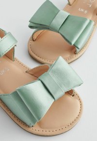 Sandali in raso verde con un grande dettaglio a fiocco, design open toe e suola in faux leather beige con accenti di cucitura. Taglia UK 6.