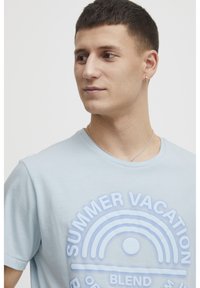 Lyse blå bomull T-skjorte med hevet grafisk print av en regnbue og teksten "SOMMERFERIE". Korte ermer og rund hals.