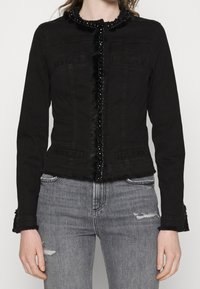 Giacca in denim nera con design aderente, dettagli in perline e pelliccia sintetica lungo il centro e al colletto, dotata di due tasche frontali e polsini sfrangiati.