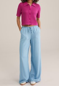 Rosa stickad kortärmad cardigan med knappar framtill, matchad med ljusblå vida byxor med elastisk midja och dragsko.