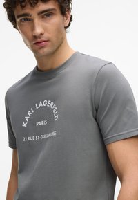 Hallh halli puuvillane t-särk, millel on ümmargune kaelus ja lühikesed varrukad. Esiküljel valge tekst "KARL LAGERFELD PARIS 21 RUE ST-GUILLAUME".