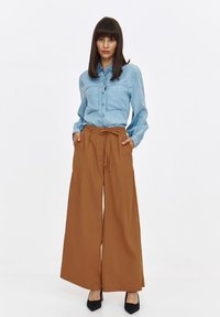Jasnoniebieska koszula dżinsowa z dwoma kieszeniami na piersi, połączona z brązowymi spodniami z wysokim stanem i szerokimi nogawkami oraz czarnymi szpilkami z ostrym noskiem.