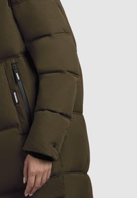 Gevoerde olijfgroene jas met een ritssluiting aan de zijkant, voorzien van een gestructureerd oppervlak en knoopdetail bij de manchetten.