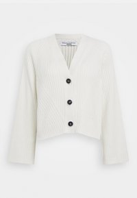 Vit räfflad kofta med djup V-ringning, kortad form och tre svarta knappar. Har strukturerade diagonala mönster på ärmar och kropp.