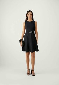 Vestido preto sem mangas com corpete ajustado e saia rodada, apresentando uma fivela prateada como detalhe. Tecido suave e design até ao joelho.