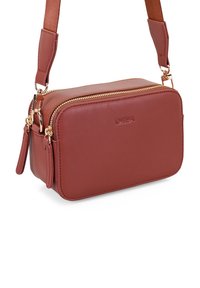 Braune Leder-Umhängetasche mit goldfarbenem Reißverschluss, rechteckiger Form, abnehmbarem Trageriemen und geprägtem Logo auf der Vorderseite.