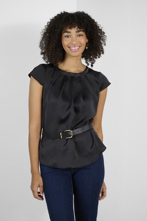 Top en satin noir avec des manches courtes, design plissé et taille ceinturée avec une boucle dorée, associé à un jean bleu foncé.