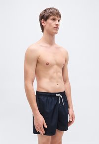 Μπλε ναυτικές βερμούδες κολύμβησης από ελαφρύ ύφασμα, με ελαστική μέση και κορδόνι, σε άνετη εφαρμογή έως το γόνατο.