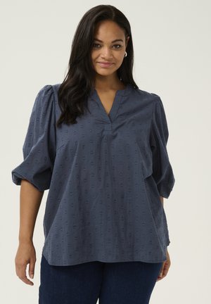 Navy blue blouse made of textured fabric featuring a V-neck, puffed sleeves, and a subtle heart pattern throughout. Loose fit.