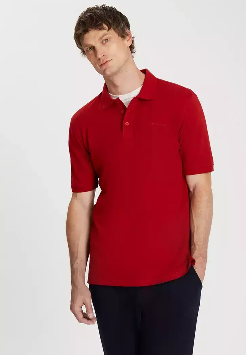 Czerwona koszulka polo z krótkim rękawem, z kołnierzykiem, z zapięciem na trzy guziki oraz subtelnym logo. Wykonana z gładkiej tkaniny w klasycznym kroju.