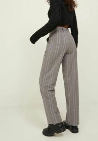 Szare i czarne spodnie w kratę o wysokim stanie z prostymi nogawkami. Posiadają teksturowany materiał oraz boczne kieszenie. Noszone z czarnymi botkami.