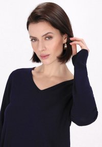 Maglione blu navy a V in tessuto morbido, con maniche lunghe. Presenta polsini aderenti e superficie texture. Modello che indossa il capo.
